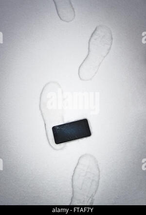Someone stepped on  a phone and damaged screen. Device in snow with foot imprints. Stock Photo