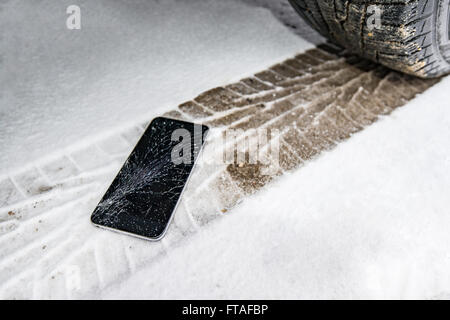 Phone with broken screen on snow in car trail. Glass covered with snow flakes. Device run over by wheel. Stock Photo