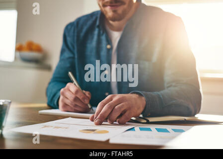 Businessman analysing statistical charts and graphs as he sits writing notes at his desk in a home office, low angle close up vi Stock Photo
