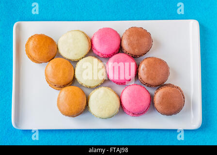 Rectangular white ceramic plate with colorful raspberry, chocolate, pistachio and coffee macarons against a cyan background. Stock Photo