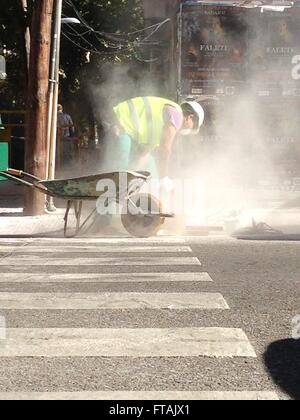 Badajoz, Spain - 23 November, 2015: worker cuts to paving stones at the end of zebra crossing rising a huge dust cloud Stock Photo