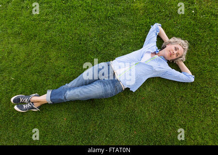 Middle-aged woman in casual weekend clothing relaxing on the grass in a backyard or park. She is smiling with a happy, contented expression. Stock Photo