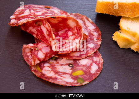 Slices of salami with pistachios on top in slate Stock Photo