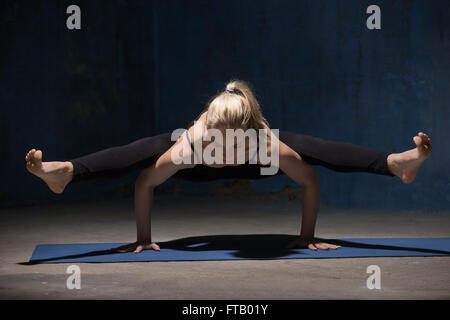 Beautiful sporty fit young woman working out indoors against grunge dark blue wall. Model doing handstand, arm balance Stock Photo