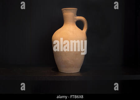Terracotta vase earthenware household item handmade on a dark shelf isolated on black, chiaroscuro style. Stock Photo