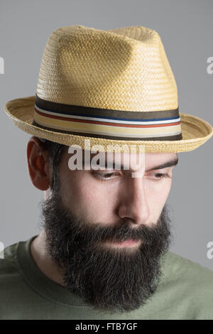 Close up portrait of bearded man wearing straw hat looking down. Headshot over gray studio background. Stock Photo