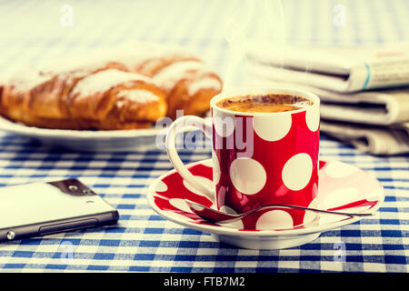 Coffee. Cup of coffee. Dotted cup of coffee, two sweet croissants, paper newspapers, mobile phone on blue checkered tablecloth. Stock Photo