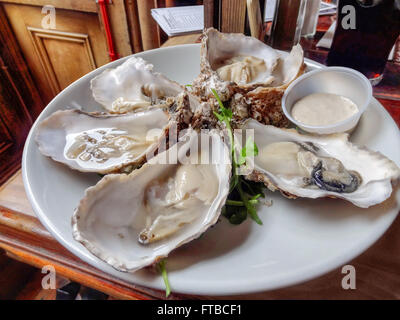 some opened oysters on a white plate with dip in wooden ambiance Stock Photo