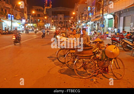 Women sell peanuts and other snacks from their bikes beside a busy street at night in Tra Vinh in the Mekong Delta, Vietnam Stock Photo