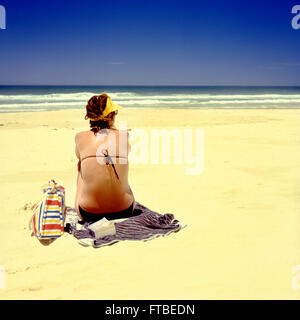 Woman in bikini sitting on sandy beach with clear blue sky. Space for text. Stock Photo