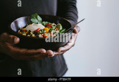 A man is holding a bowl of Mexican Burrito Bowl topped with cashew chipotle cream sauce. Stock Photo
