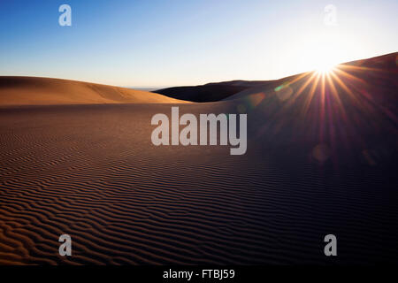 Sunlight peaking over sand dune in remote desert.  Great Sand Dunes National Park, Colorado, USA. Stock Photo