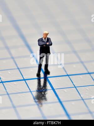Miniature figurine businessman with arms folded standing on a  blue squared shiny surface. Stock Photo