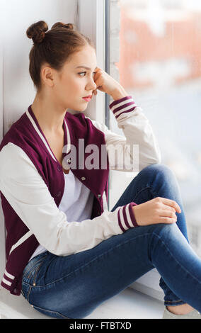 sad pretty teenage girl sitting on windowsill Stock Photo