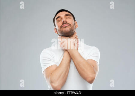 young man choking himself over gray background Stock Photo