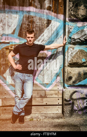 Attractive young man standing against colorful graffiti wall, looking at camera. Full length shot Stock Photo