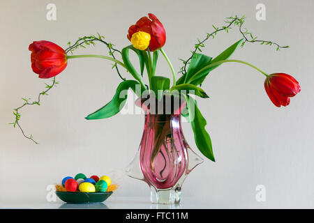 Flowering tulips in vase white background and colored Easter eggs Stock Photo