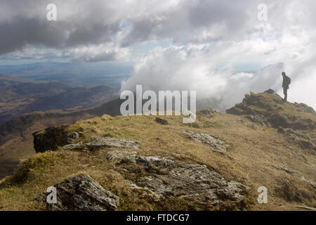 A walker admires the view as clouds flow over the Crib Goch Ridge while descending, Snowdon along the Rhyd Ddu Path, Snowdonia. Stock Photo