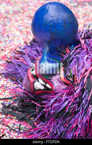 A single mask of a Waggis with a huge blue nose and pink-purple hair laying on the ground on top of colorful confetti. Stock Photo