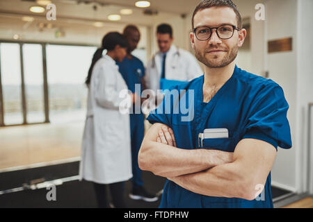 Confident relaxed surgeon doctor at hospital with team of doctors in background Stock Photo