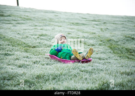 A little boy sledging on frosty grass without proper snow Stock Photo