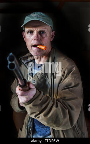 a-man-pointing-a-shotgun-with-a-spare-cartridge-in-his-mouth-ftdr6w.jpg