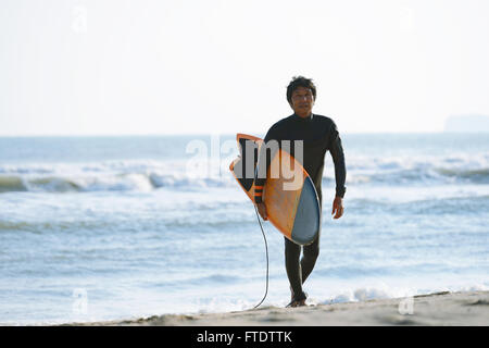 Japanese surfer walking on the beach Stock Photo