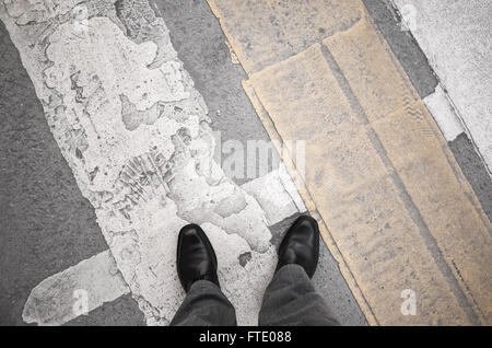 Urbanite man in black new shining leather shoes standing on the dirty pedestrian crossing road marking Stock Photo