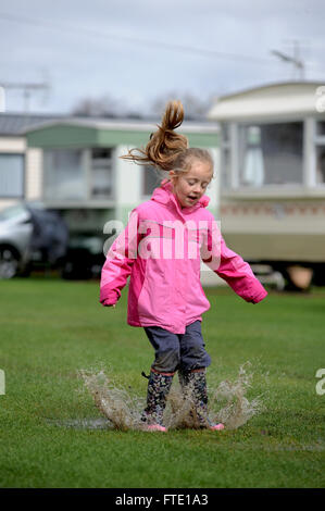 A little girl enjoys jumping in a puddle left by Storm Katie at a caravan site in York, North Yorkshire, UK. Stock Photo