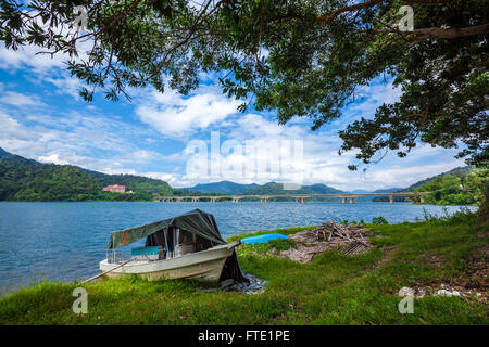 Boat on shore of a tropical lake and islands in cloudy blue sky. Belum resort, Banding, Temenggor Lake. Malaysia Stock Photo