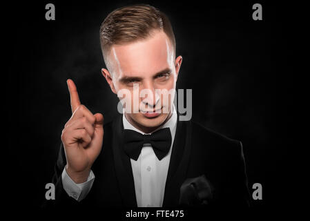 Idea. Young man shows finger up over darck background. Stock Photo