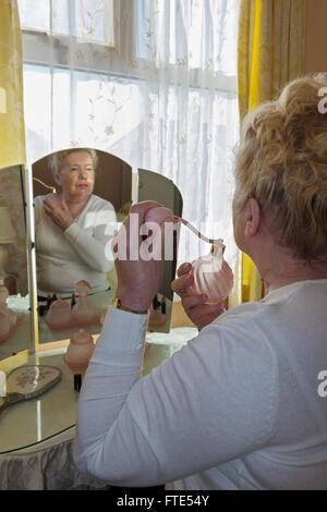 Elderly lady sat at an old fashioned dressing table applying perfume. Stock Photo