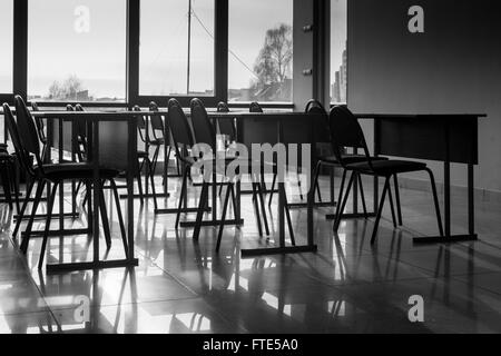 Rows and lines of empty conference chairs caught in natural sunlight in a classroom school environment. Black and white image wi Stock Photo