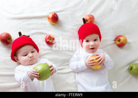 two cute babies lying in hats on soft blanket with apples Stock Photo