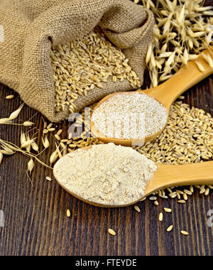 Flour and oat bran in two spoons, bag with oat and stalks of oats on the background of wooden boards Stock Photo