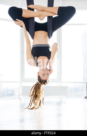 Cheerful young woman doing aerial yoga and talking on mobile phone in stusio Stock Photo