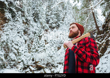 Portrait of handsome bearded young man with axe in winter forest Stock Photo