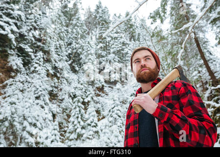 Serious bearded young man holding axe and walking in winter forest Stock Photo
