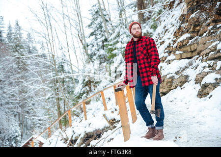 Thoughtful attractive young man with beard standing and holding axe in mountains in winter Stock Photo