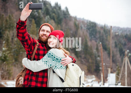 Happy young couple making selfie photo on smartphone outdoors with forest on background Stock Photo