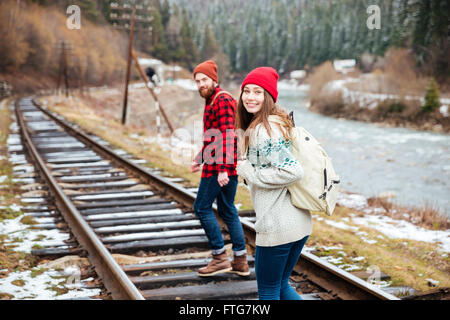 Happy young couple with backpacks walking along railroad Stock Photo