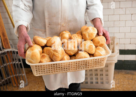 Baker holding a basket full of freshly baked crusty white bread rolls in his white coat at the bakery Stock Photo