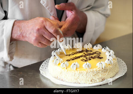 Close Up of Male Baker Writing Celebratory Message on Top of Lemon Cake Stock Photo
