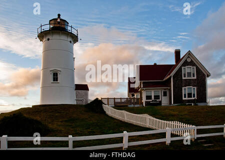 Sun sets behind Nobska lighthouse on Cape Cod and keepers building on a warm summer evening. Stock Photo