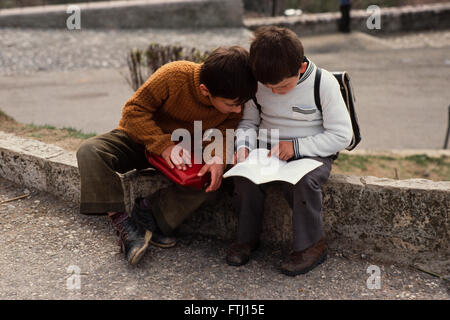 Two boys dicussing their homework, sit on a kebstone in Gjirokaster, Albania Stock Photo