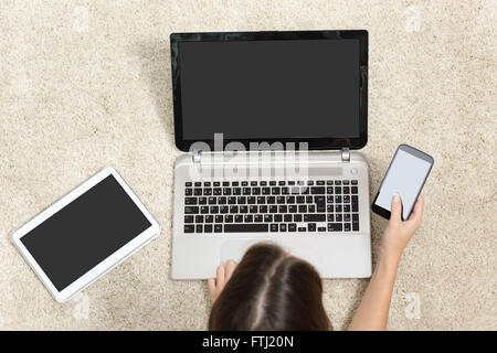 Woman working with multiple device screens lying on the floor at home Stock Photo