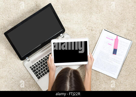 Top view of a girl studying with laptop and tablet showing blank screens lying on a carpet at home Stock Photo
