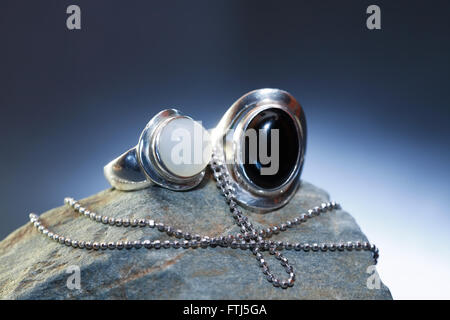 Silver rings with gem near chain on gray stone against nice dark background Stock Photo
