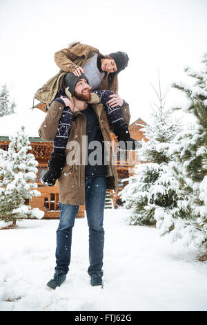 Cheerful young woman sitting on man shoulders and laughing in winter Stock Photo