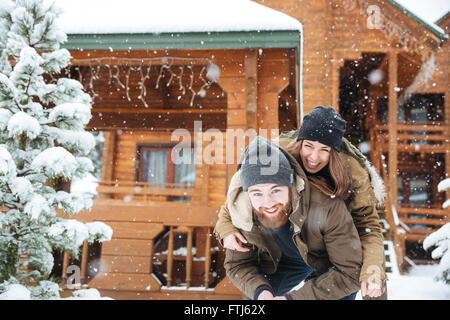 Beautiful cheerful young couple having fun in front of log cabine in winter Stock Photo
